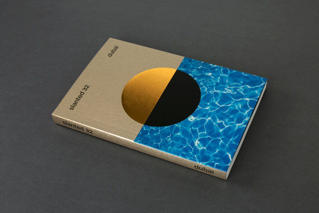 Magazine lying flat on a surface containing issue 32 of Slanted magazine, focusing on Dubai. The magazine cover has a metallic finish in a half-and-half split image design.  
